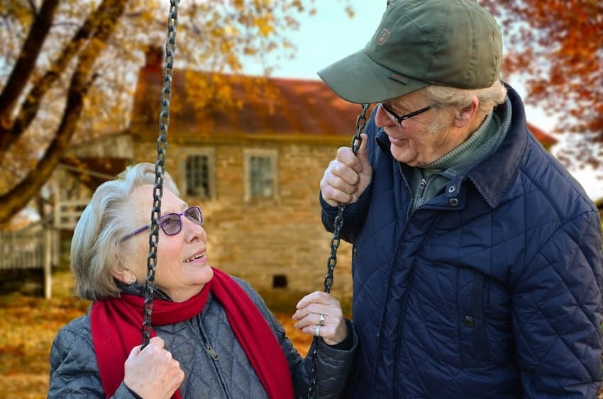 Seniorenimmobilie für die Selbstnutzung gefunden - dann ist die Freude groß: älteres Paar auf Schaukel vor Haus
