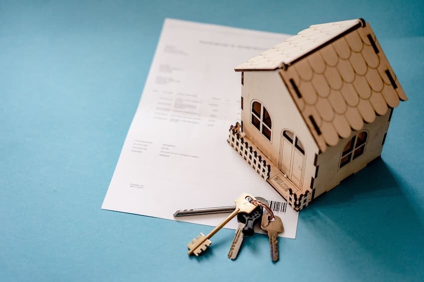 Immobilien als Altersvorsorge: Bild zeigt kleines Modellhaus mit Hausschlüssel auf einem Tisch
