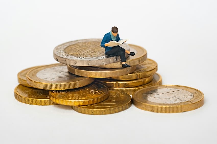 Anschlussfinanzierung: was Verbraucher beachten sollten - auf einem Münzstapel sitzt eine männliche Figur und liest Zeitung